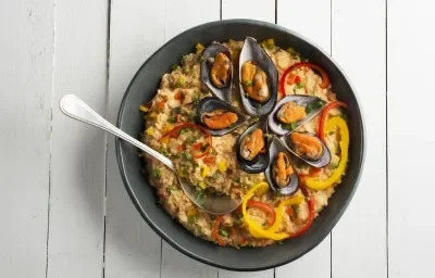 Una fotografía en blanco y negro de una encimera blanca, con un plato negro de arroz con mariscos y una cuchara encima.