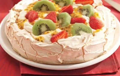 Una fotografía en tonos rojos muestra una encimera con un mantel rojo, un plato blanco con Pavlova y una cuchara al fondo.