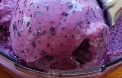 Fotografía de una masa de helado de uva morada elaborada en un robot de cocina, sobre una encimera de madera.
