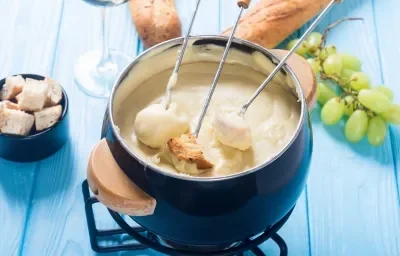 Foto da Receita de Fondue de Queijo Sem Lactose. Observa-se uma panelinha de fondue azul com três espátulas de pão dentro. Foto da Receita de Fondue de Queijo Sem Lactose. Observa-se uma panelinha de fondue azul com três espátulas de pão dentro.