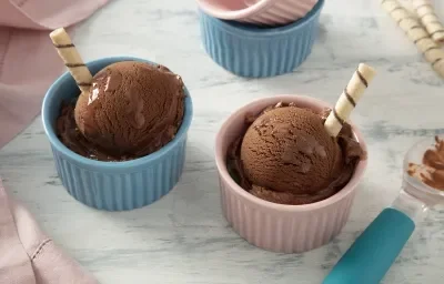 Foto de la receta de Helado de MOÇA con Nescau. Se pueden ver dos botes individuales, uno rosa y otro azul, uno con cada bola de helado. Cada bote tiene una barra de oblea.