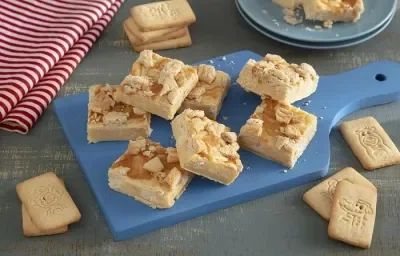 Foto en tonos beige de la receta de dulce para microondas hecho con galletas "Passo", servida en varias porciones sobre una tabla azul con algunas galletas "Passo" de leche alrededor. Al fondo, un mantel a rayas rojas y blancas y un plato azul.