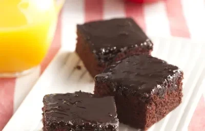 Foto con 3 piezas cuadradas de tarta Nescau y glaseado Nescau. En la parte inferior de la foto, hay un frasco con jugo de naranja y 2 manzanas en un plato rojo. Foto con 3 piezas cuadradas de tarta Nescau y glaseado Nescau. En la parte inferior de la foto, hay un frasco con jugo de naranja y 2 manzanas en un plato rojo.