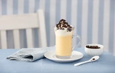 fotografia em tons de azul e branco de uma bancada azul vista de frente, contém um pratinho redondo branco com um copo transparente com a bebida dentro e por cima chantilly e biscoitos triturados para decorar. Ao lado um pano azul e do outro uma colher. fotografia em tons de azul e branco de uma bancada azul vista de frente, contém um pratinho redondo branco com um copo transparente com a bebida dentro e por cima chantilly e biscoitos triturados para decorar. Ao lado um pano azul e do outro uma colher.