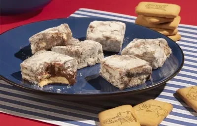 Fotografía en tonos azules y rojos de una encimera roja con un mantel a rayas azules y blancas, sobre el cual hay un plato azul oscuro con pajitas de galleta italiana. Galletas y leche esparcidas al fondo.