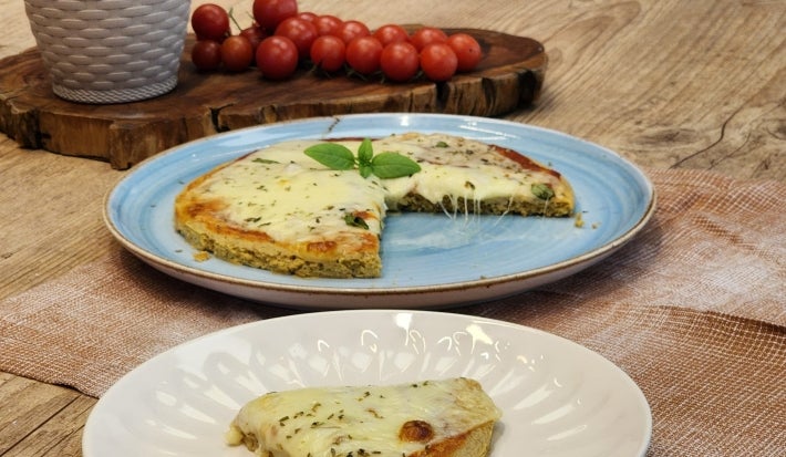 Fotografía en tonos marrones con un plato azul en el centro. Sobre el plato hay una pizza de avena con queso mozzarella y orégano.