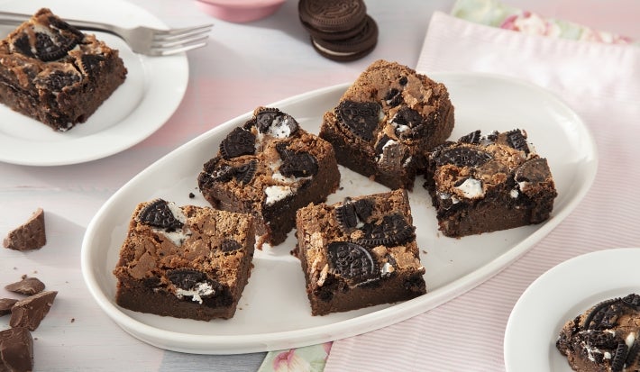 Foto de la receta de Brownie con Leche Condensada y Galletas Negresco. Muestra 7 rebanadas de brownie cortadas y dispuestas en un molde ovalado blanco sobre un fondo rosa pastel. Foto de la receta de Brownie con Leche Condensada y Galletas Negresco. Muestra 7 rebanadas de brownie cortadas y dispuestas en un molde ovalado blanco sobre un fondo rosa pastel.