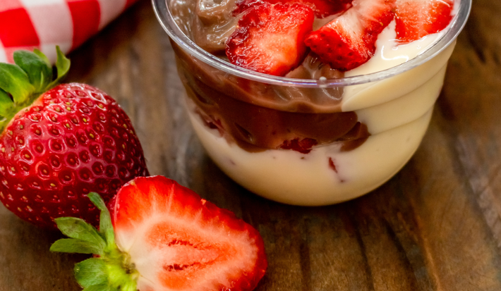 Fotografía de un frasco transparente que muestra capas de pastel de cacao, salsa de proteína cremosa con fresas.