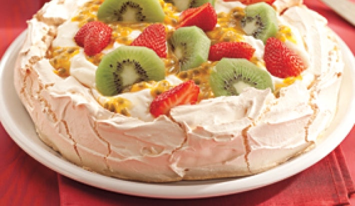 Una fotografía en tonos rojos muestra una encimera con un mantel rojo, un plato blanco con Pavlova y una cuchara al fondo.