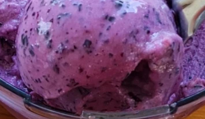Fotografía de una masa de helado de uva morada elaborada en un robot de cocina, sobre una encimera de madera.